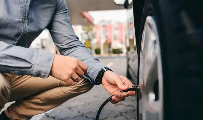 شخص يقوم بتعبئة هواء إطار سيارة باستخدام خرطوم الهواء عند محطة وقود، للتحقق من وضبط ضغط الإطارات قبل القيادة في أجواء حارة.