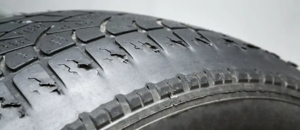 لقطة قريبة لإطار سيارة متشقق ومتآكل، مع ظهور تلف في نقشة المداس، ما يدل على انتهاء عمر الإطار والحاجة إلى استبداله خاصة في الأجواء الحارة.