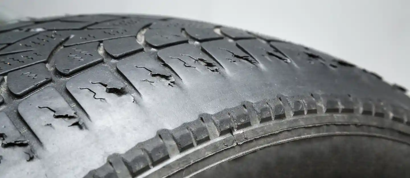 لقطة قريبة لإطار سيارة متشقق ومتآكل، مع ظهور تلف في نقشة المداس، ما يدل على انتهاء عمر الإطار والحاجة إلى استبداله خاصة في الأجواء الحارة.