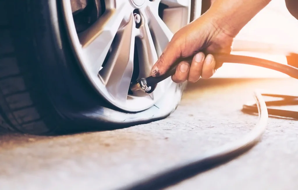 إطار سيارة مفرغ من الهواء على طريق في الرياض مع توصيل خرطوم هواء لفحص أو نفخ الإطار تحت حرارة الجو